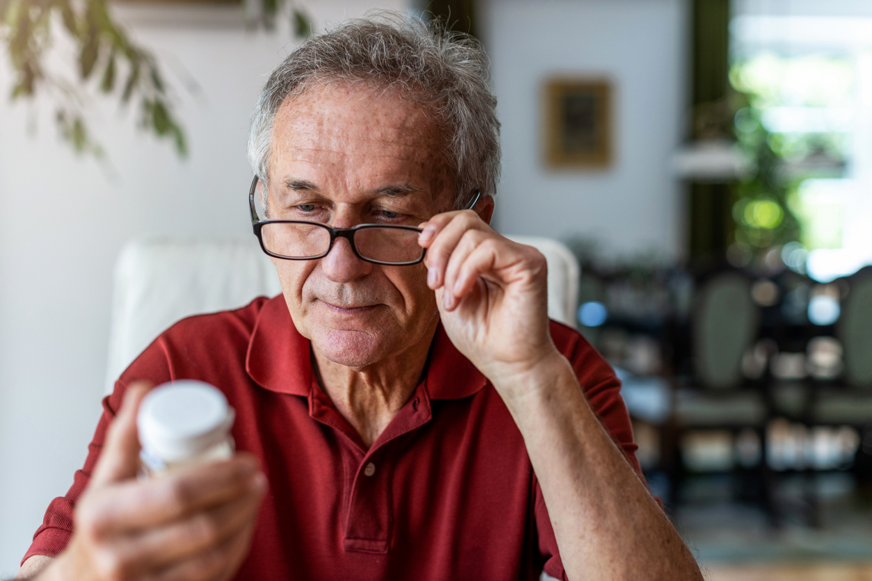 Oudere man met leesbril bekijkt aandachtig een potje met medicijnen.